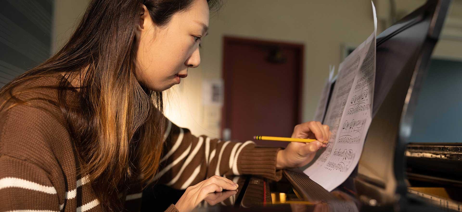 A student sits at a piano annotating 音乐 with a pencil