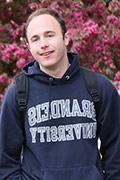 A student wearing a Brandeis sweatshirt, pink cherry blossoms are in bloom in the background.
