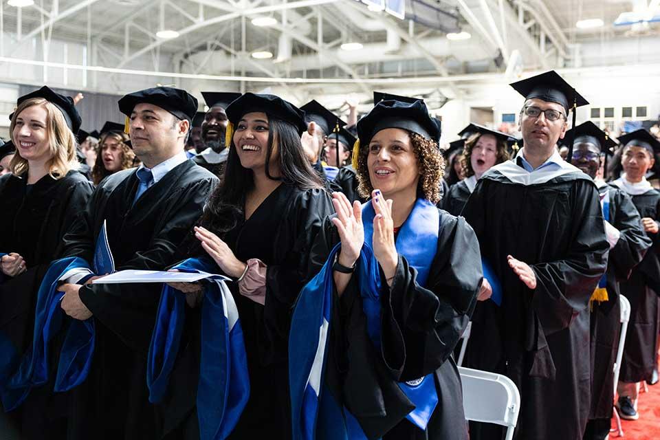 Students in caps and gowns clap during the Graduate Commencement Ceremony